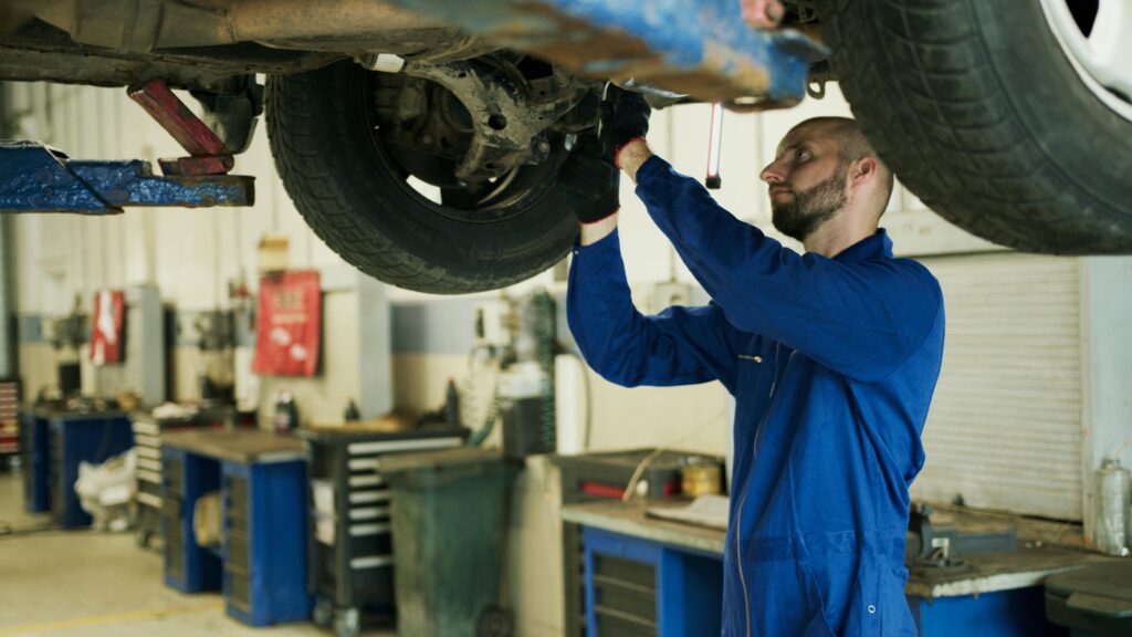 pexels-photo-8985606-8985606 Mechanic in blue overalls inspecting vehicle undercarriage in a professional workshop.